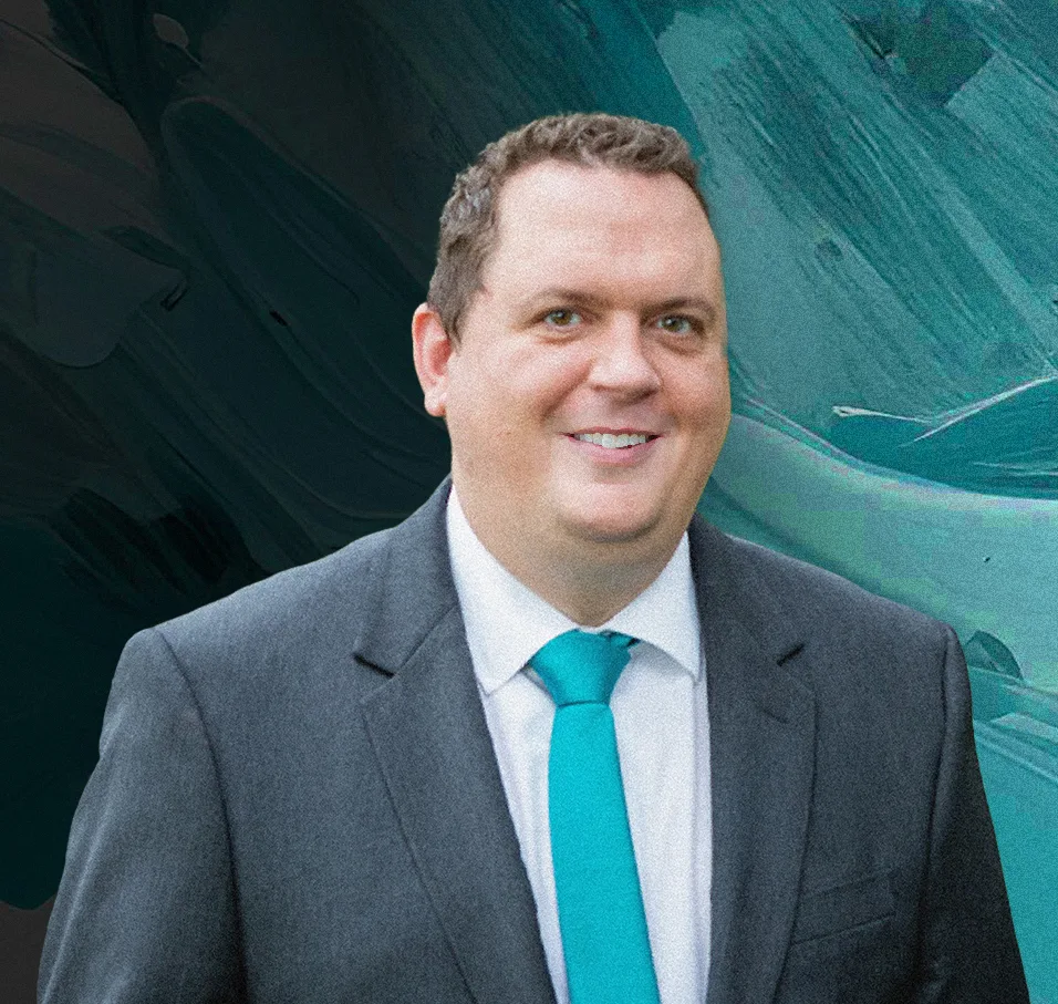 Joe Kovalck Jr., smiling, in a charcoal suit and teal tie against a painted teal background